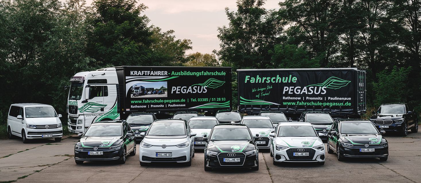 Eine Flotte von Fahrschulfahrzeugen der Pegasus-Fahrschule, darunter Autos, ein Van und ein Lkw, steht auf einem Parkplatz mit Bäumen im Hintergrund